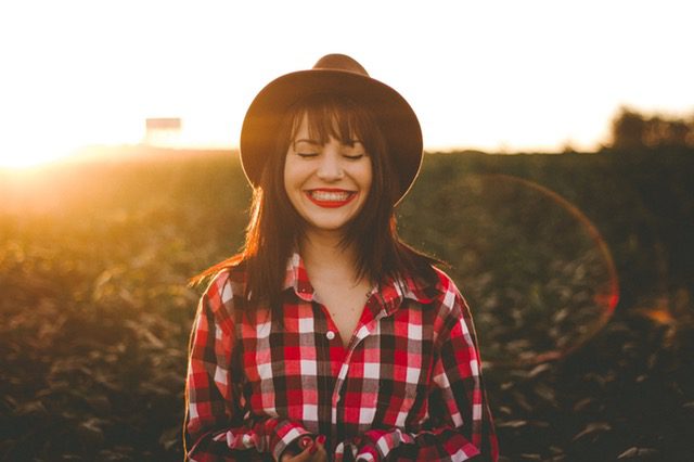 Smiling woman wearing a hat and flannel plaid shirt.