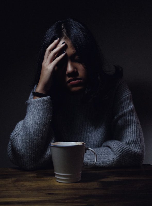 Woman wearing a blue sweater, holding her head and looking ill.