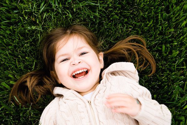 Smiling girl with brown hair laying on green grass.