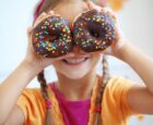 young child holding 2 donuts up over their eyes