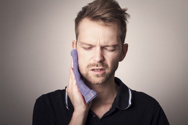 Man with a toothache holding a purple cloth against his cheek.